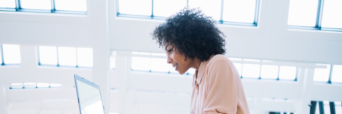 Black smiling female entrepreneur typing documentation for software application on laptop, prosperous owner of business working on netbook using wifi connection sitting in financial buildings