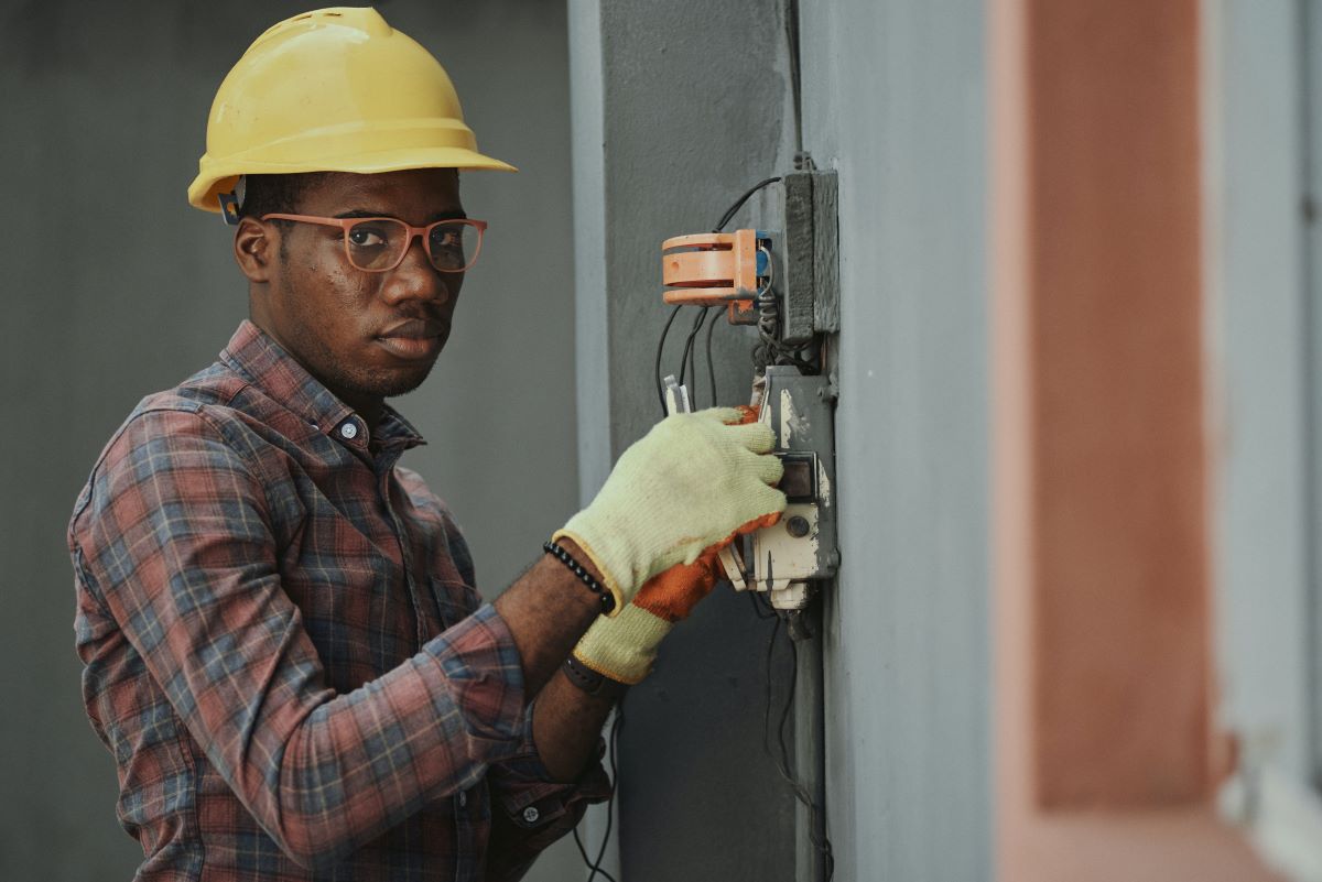 An electrician in a hardhat working on a fuse box.