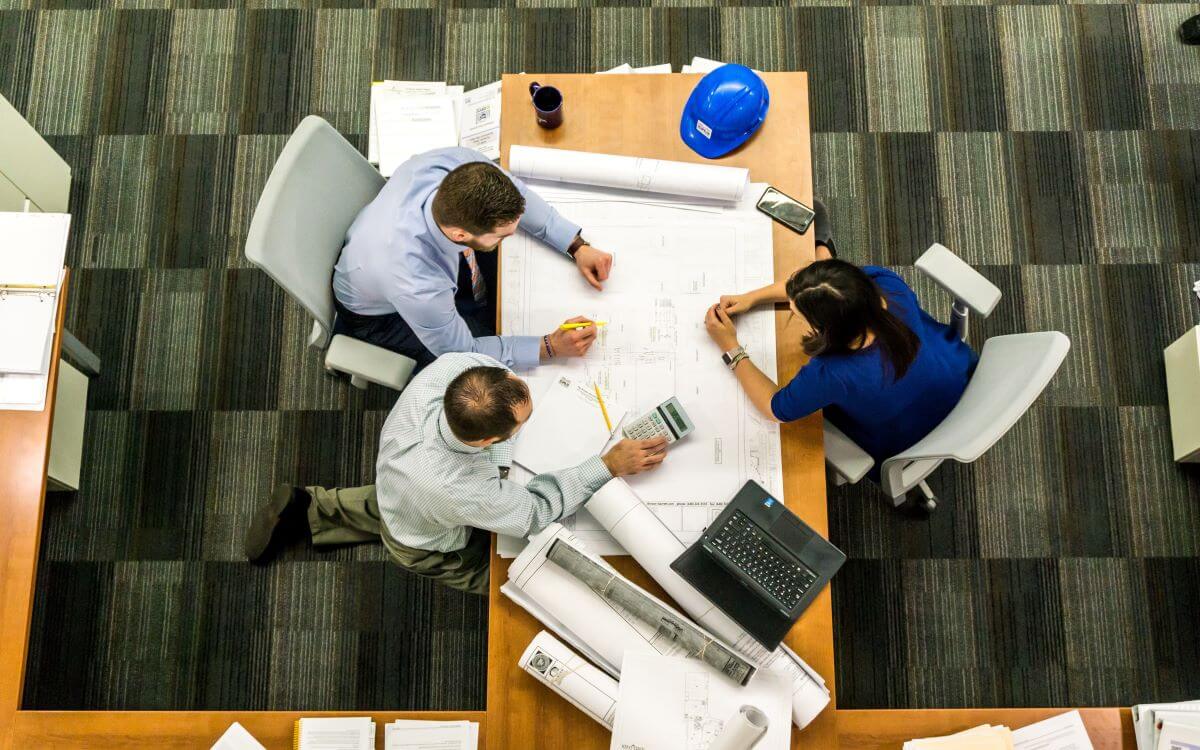 A top-down view of three people working around a cluttered desk.