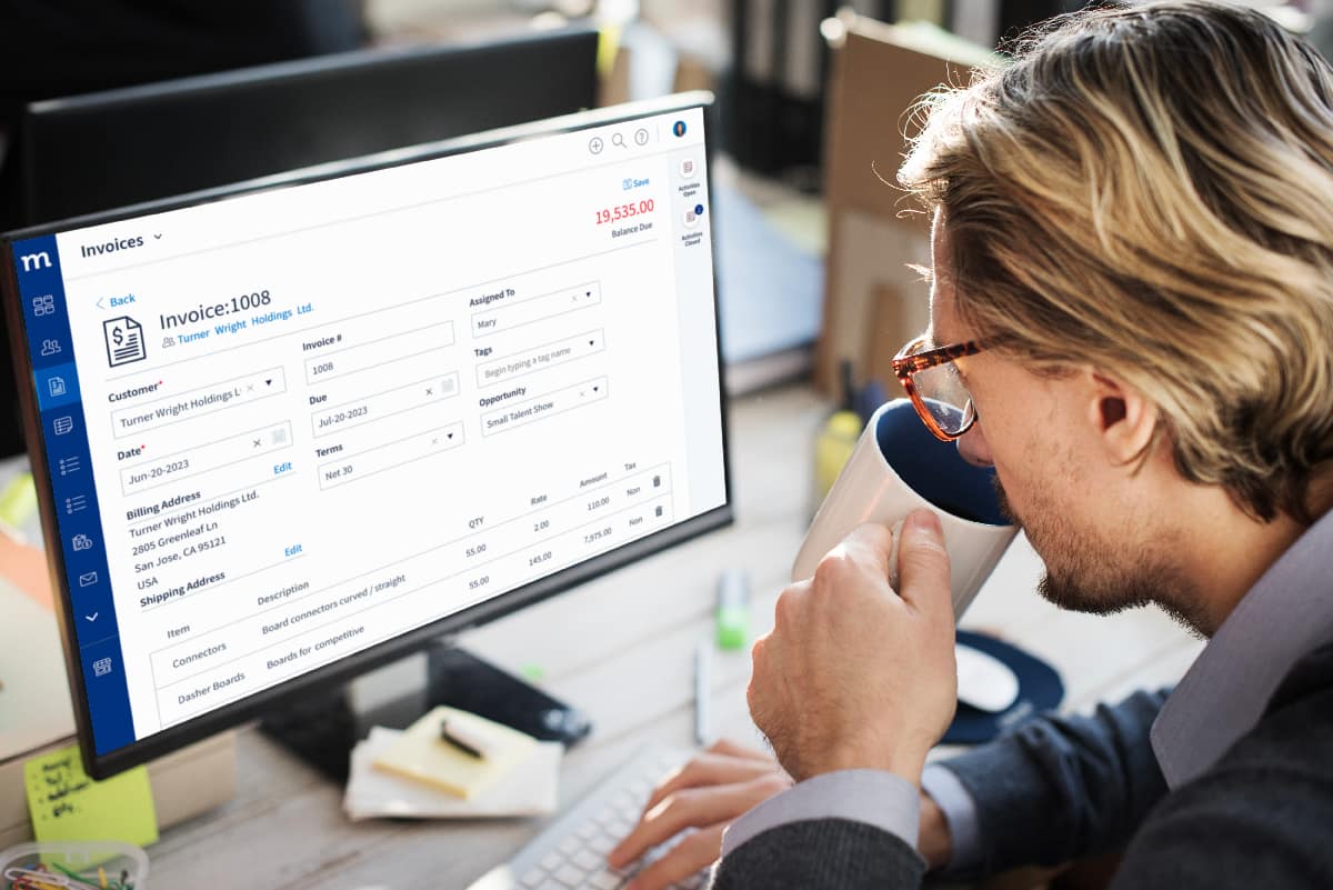 Blonde man sipping on a mug while looking at a screen that displays a QuickBooks Online invoice template