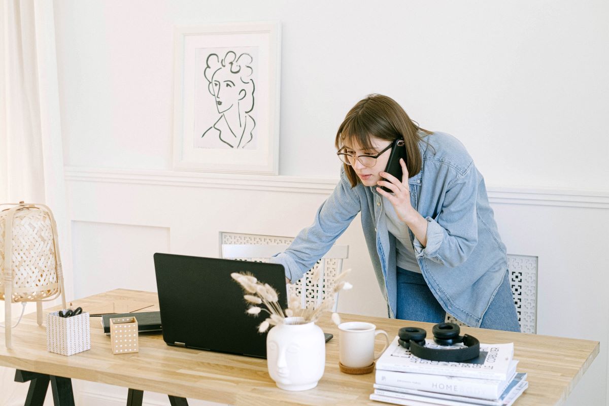 A woman talking on a phone and looking at a laptop.