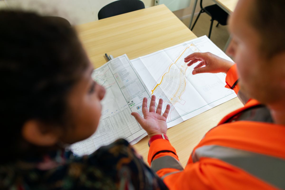 Two people in work clothes having a discussion over schematics.