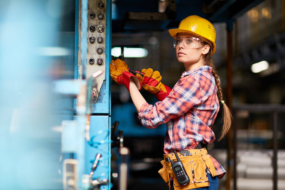 A technician in safety gear working on a piece of equipment with a screwdriver.