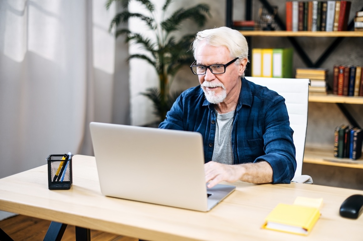 Mature gray-haired man using laptop computer sitting at home office