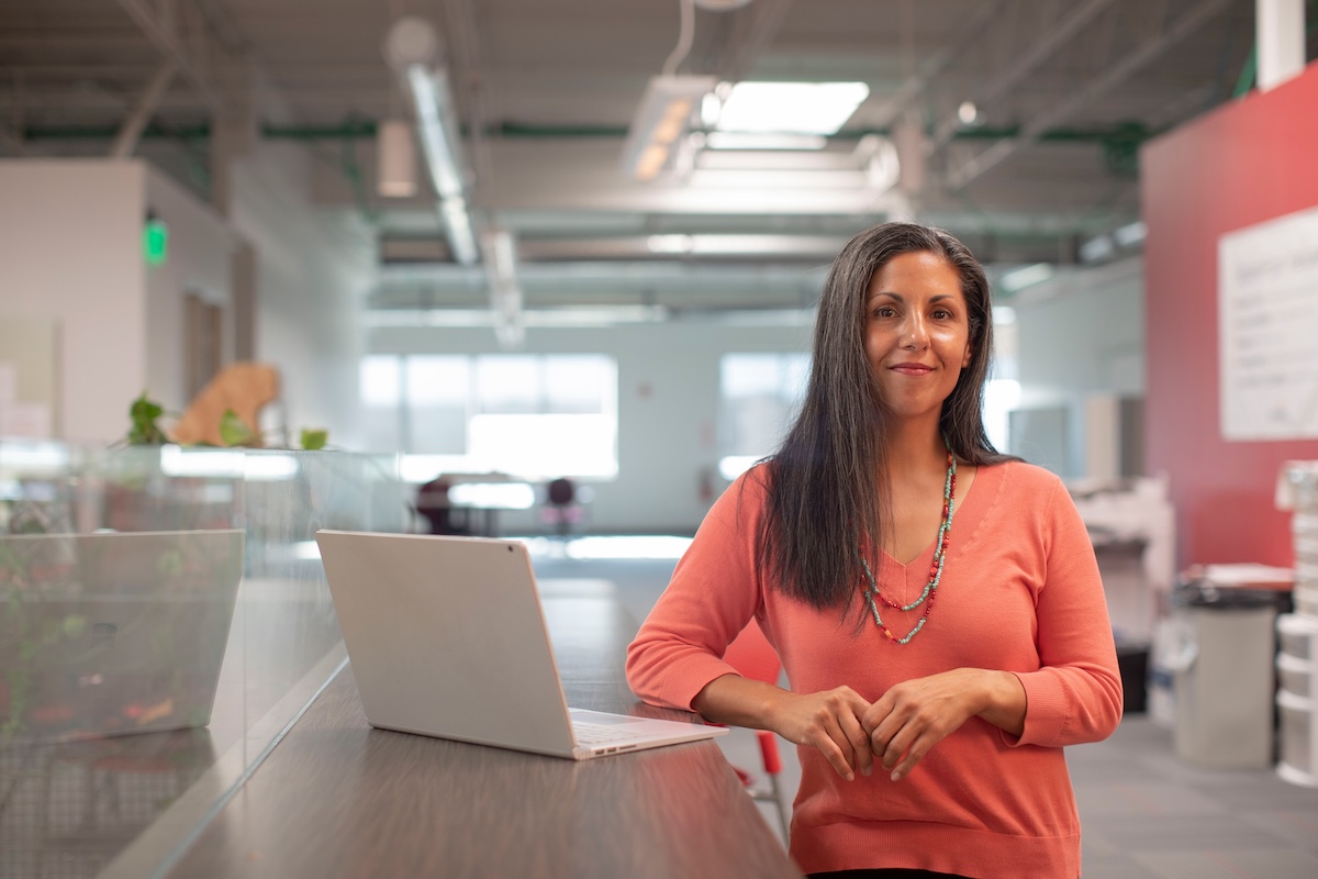 Woman smiling while leaning on desk with computer