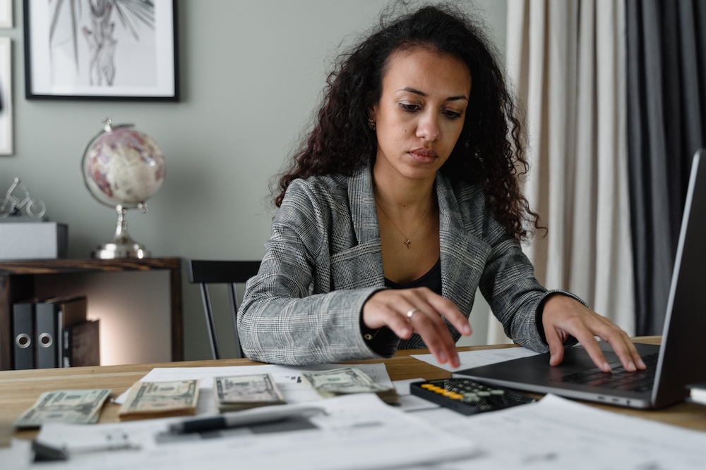 Woman counts money on desk with computer and calculator