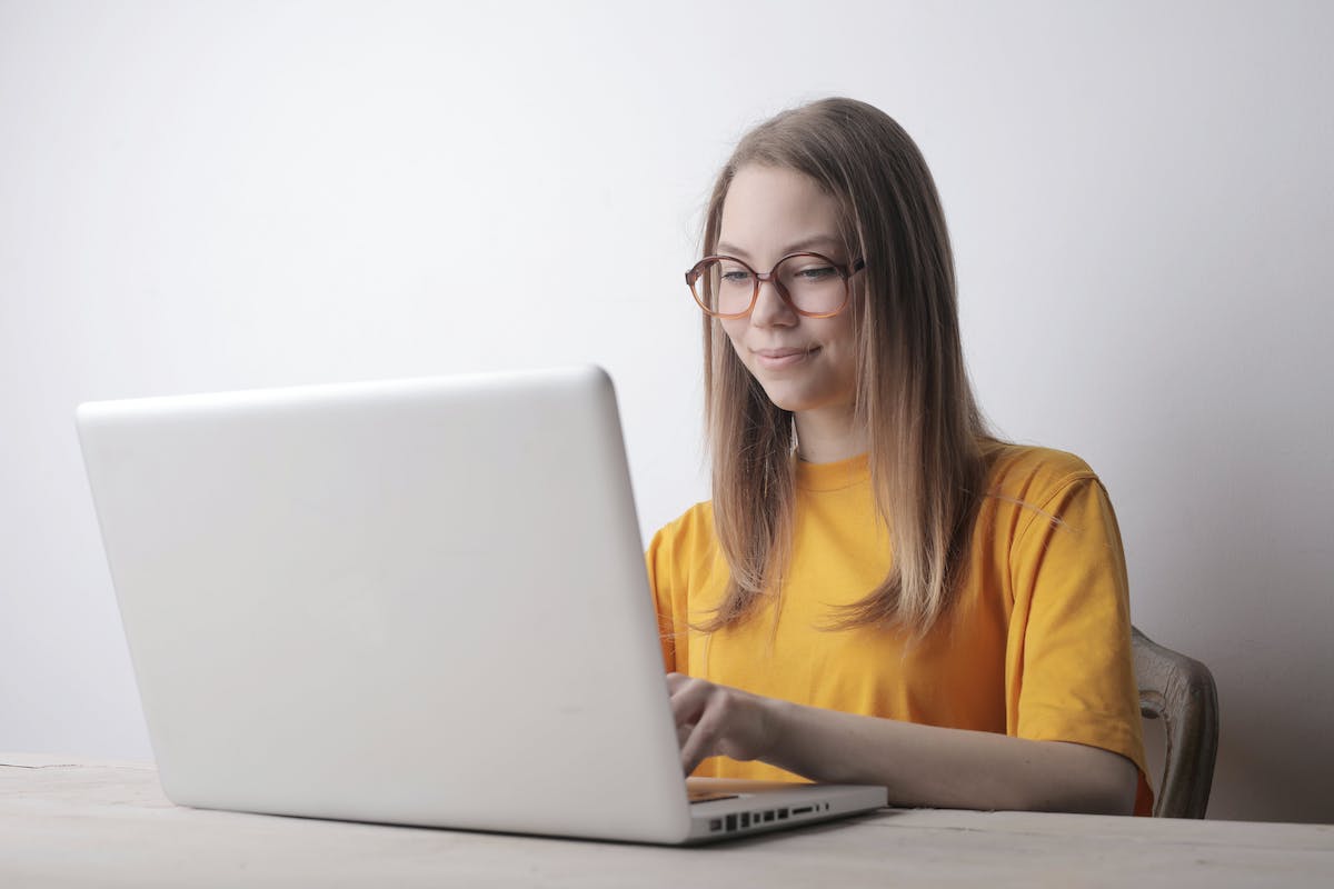 Woman in yellow crew-neck t-shirt wearing eyeglasses using laptop