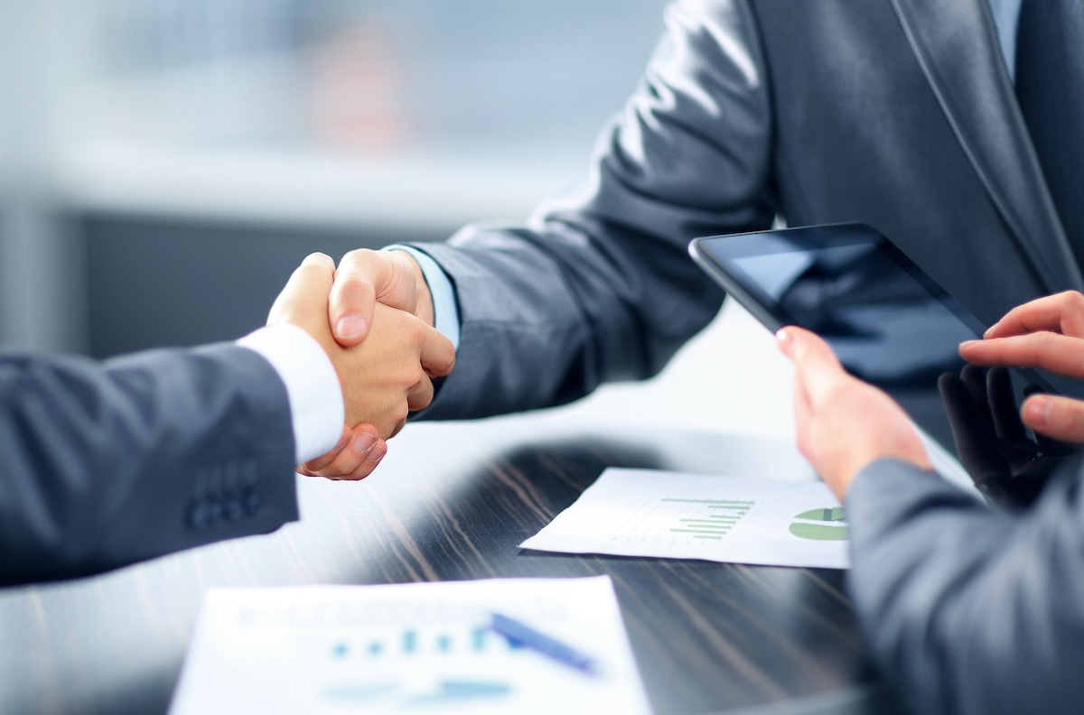 Two people shaking hands over documents on desk.