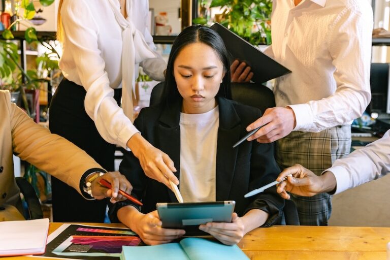 Woman holding tablet while co-workers point at elements on its screen.