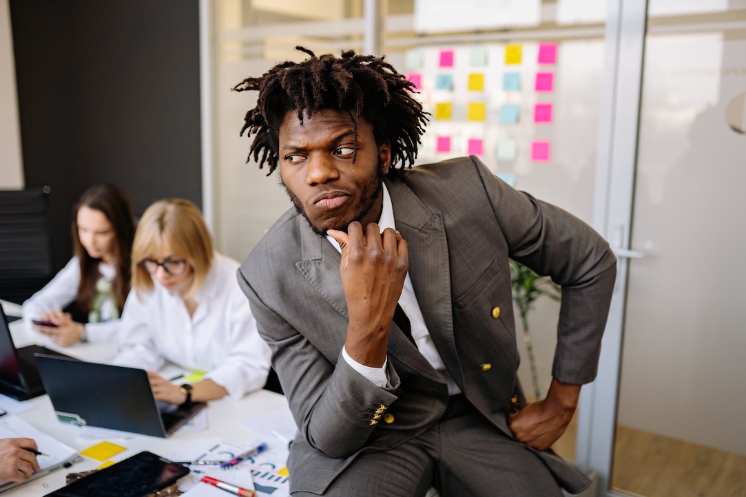 Man on desk thinking while his team works in the background.