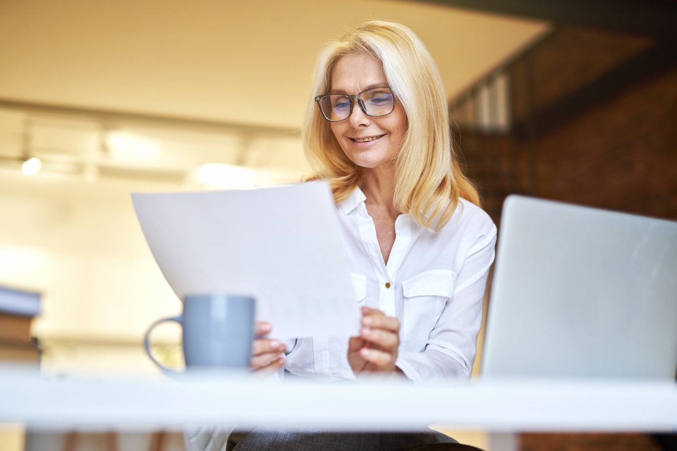 Successful mature businesswoman in glasses smiling, using laptop and doing some paperwork at the office. People, business, career concept