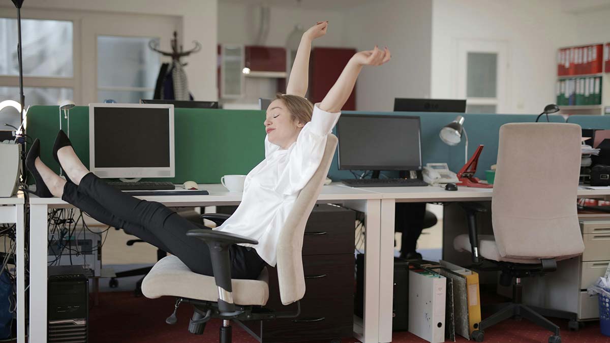 A woman sitting in an office stretching her arms and legs out.