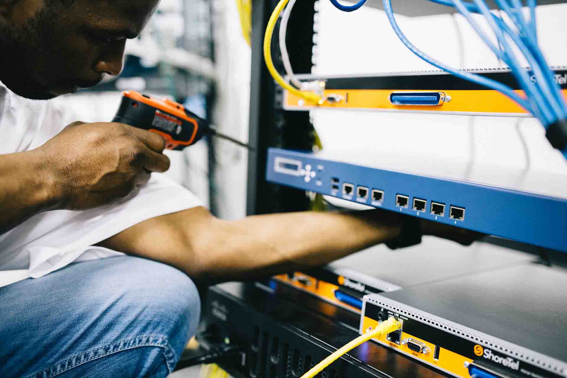 A field engineer holding a tool to a rack of hardware.