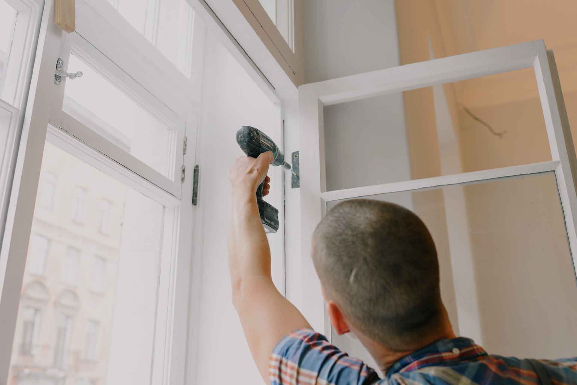 A man drilling into the frame of a window.