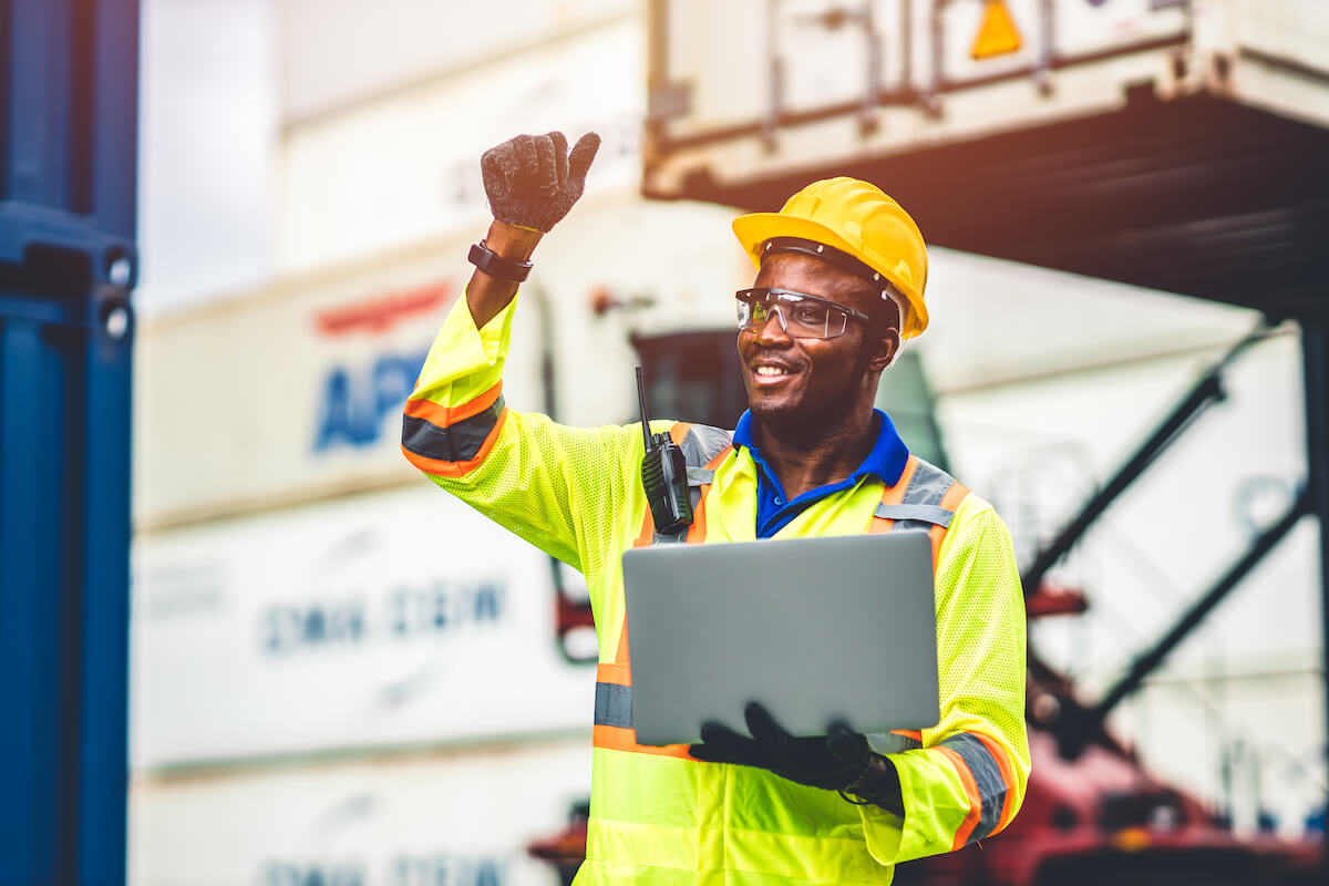 A construction worker holding a laptop, smiling, and giving a thumbs up.