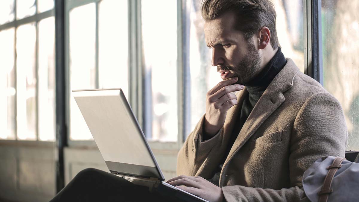 A thinking man sitting with a laptop on his lap.