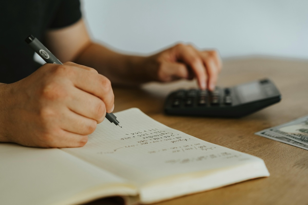 Person writing on notebook and using calculator