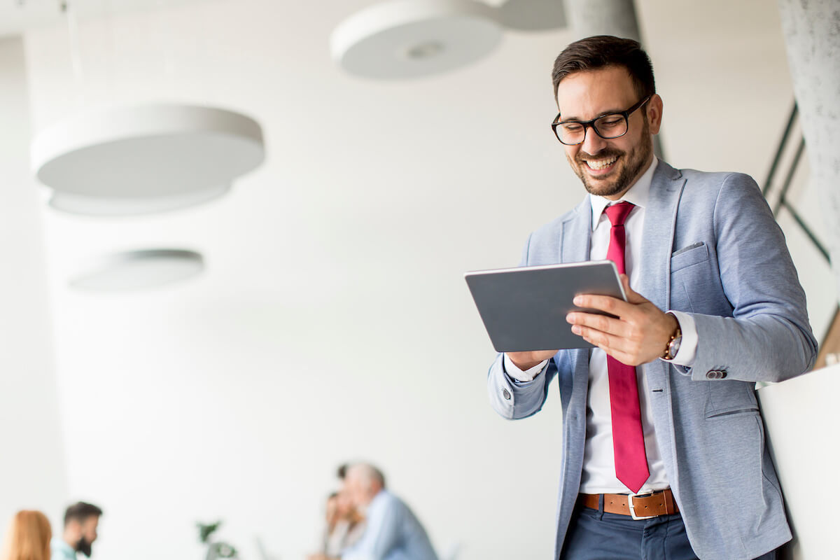 A man in a suit and tie smiling while using a tablet.