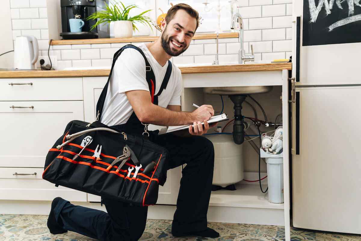 A plumber working underneath a sink and smiling.