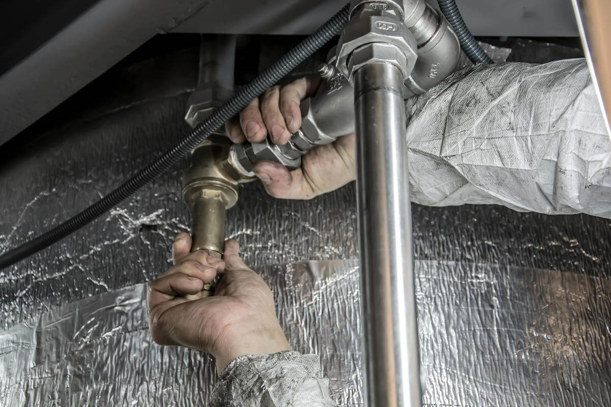 A closeup of a plumber working on a pipe under a sink.