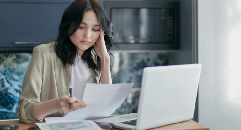 A woman seated in front of a laptop reading over a document.